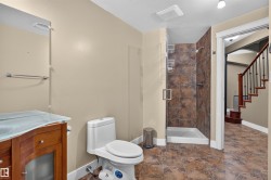 Full bathroom with a tiled walk-in shower, wood-finish vanity with a glass countertop, and patterned floor tiling - 
