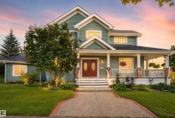 Two-story residence featuring a covered front porch, dual front entry doors, a concrete walkway, and a landscaped front yard with mature trees - 