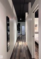 Hallway with wood-finish flooring, white walls, and a black ceiling - 