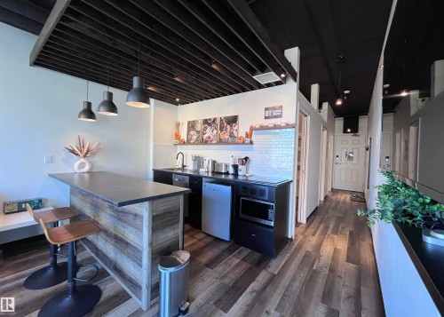 Kitchenette featuring wood-finish flooring, white subway tile backsplash, dark countertops, and three pendant lights - #1701 10024 Jasper Av Nw, Edmonton, AB 
