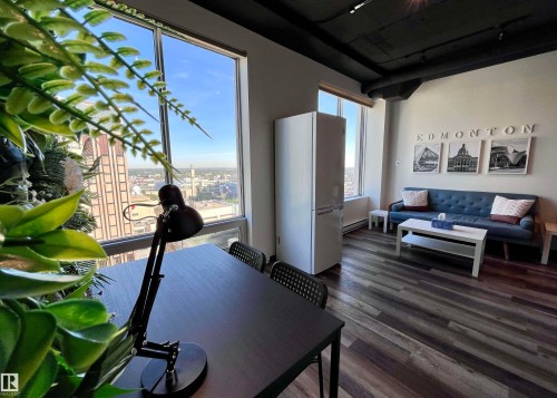 Expansive windows with city backdrop, wood-finish flooring, white walls, and exposed dark ceiling elements - #1701 10024 Jasper Av Nw, Edmonton, AB 