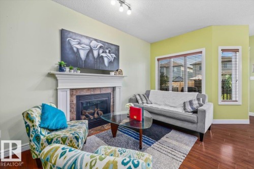 Warm living space featuring wood-finish flooring, a fireplace with a mantel, and multiple windows with blinds - 11506 17 Avenue Sw, Edmonton, AB 