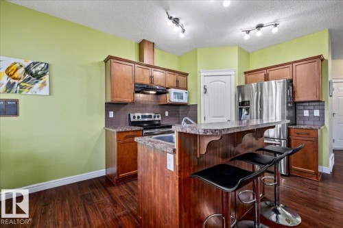 Wood-finish flooring, wood cabinetry, stone-finish countertops, stainless steel appliances, and a tile backsplash - 11506 17 Avenue Sw, Edmonton, AB 