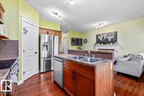 Kitchen featuring a center island with double basin sink, stainless steel appliances, wood-finish flooring, and a tiled backsplash - 11506 17 Avenue Sw, Edmonton, AB 