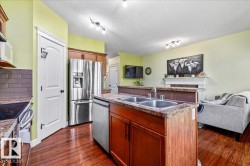 Kitchen featuring a center island with double basin sink, stainless steel appliances, wood-finish flooring, and a tiled backsplash - 