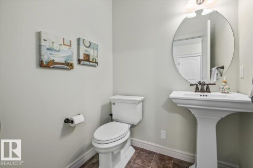 Pedestal sink with a bronze-finish faucet, oval mirror, and a white toilet - 11506 17 Avenue Sw, Edmonton, AB 
