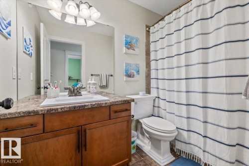 Bathroom featuring a wood-finish vanity with a built-in sink, a speckled countertop, and a shower with tiled walls - 11506 17 Avenue Sw, Edmonton, AB 