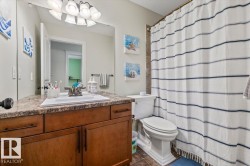Bathroom featuring a wood-finish vanity with a built-in sink, a speckled countertop, and a shower with tiled walls - 