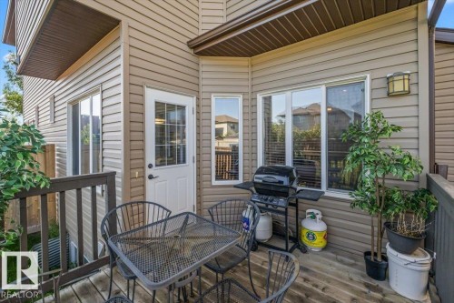 Wood-finish deck with dark-stained railing, beige siding, and multiple windows - 11506 17 Avenue Sw, Edmonton, AB 