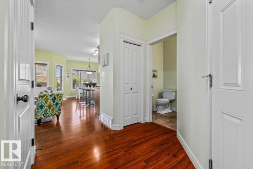 Wood-finish flooring throughout, with a paneled white door, and a partially visible powder room with a toilet and tiled flooring - 11506 17 Avenue Sw, Edmonton, AB 