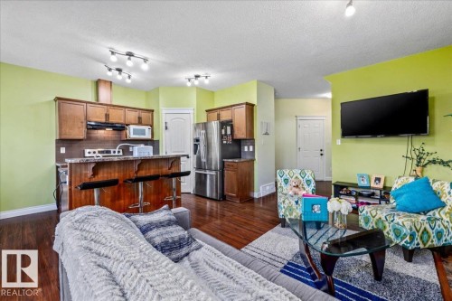 Wood-finish flooring throughout, track lighting, kitchen with wood cabinetry, stainless steel appliances, and a breakfast bar - 11506 17 Avenue Sw, Edmonton, AB 