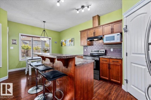 Wood-finish flooring, central island with countertop seating, rich wood cabinetry, subway tile backsplash, and a built-in microwave - 11506 17 Avenue Sw, Edmonton, AB 