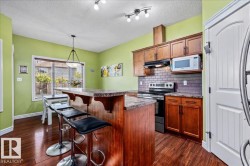 Wood-finish flooring, central island with countertop seating, rich wood cabinetry, subway tile backsplash, and a built-in microwave - 