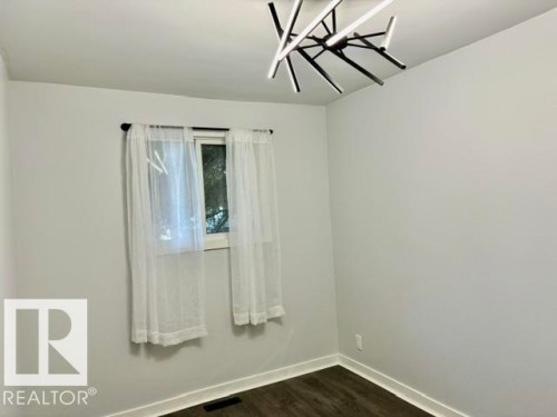 Modern ceiling fixture, wood-finish flooring, light-toned walls, and a window with sheers - 5614 50 Street, Vegreville, AB 