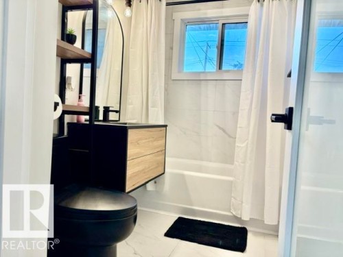 Modern bathroom featuring a black floating vanity with wood-finish drawers, white tiled walls, and a black toilet - 5614 50 Street, Vegreville, AB 