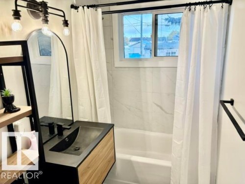 Built-in bathtub with subway tile surround, sleek wood-finish vanity with integrated sink, and an arched mirror - 5614 50 Street, Vegreville, AB 