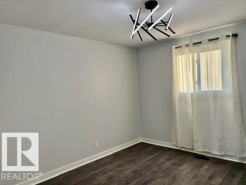 Wood-finish flooring with white trim, light gray walls, and a modern black and white ceiling fixture - 5614 50 Street, Vegreville, AB 