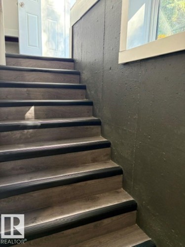 Wood-finish stairs with dark tread accents, textured wall, and natural light from a window - 5614 50 Street, Vegreville, AB 