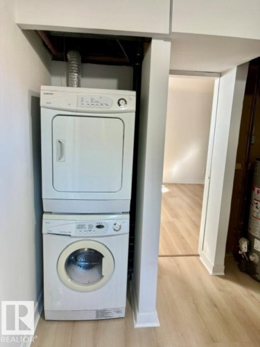 Stacked washer and dryer unit, wood-finish flooring, and white painted walls - 5614 50 Street, Vegreville, AB 