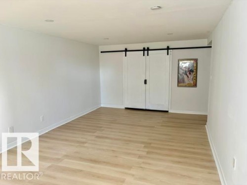 Recessed ceiling lighting, light wood-finish flooring, white walls, and white barn doors with black hardware - 5614 50 Street, Vegreville, AB 