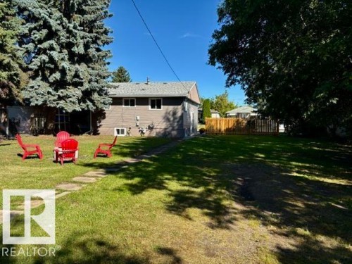 Expansive backyard featuring a manicured lawn, stone pathway, and mature trees - 5614 50 Street, Vegreville, AB 