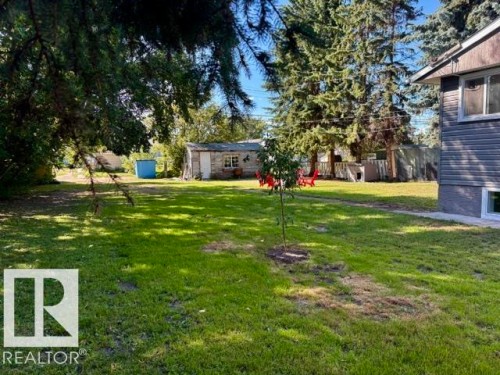 Expansive grassy yard with mature trees, a detached stone-clad outbuilding, and a separate storage structure - 5614 50 Street, Vegreville, AB 