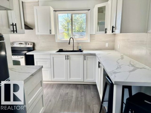White shaker cabinetry, light-toned wood-finish flooring, white countertops with grey veining, a stainless steel range, and a dark sink with a gooseneck faucet - 5614 50 Street, Vegreville, AB 