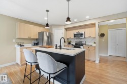 Kitchen featuring a central island with an undermount sink, pendant lighting, stainless steel appliances, and light wood-finish flooring - 