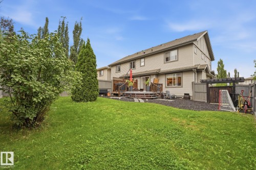 Expansive grassy yard with mature shrubs and trees, leading to a multi-level wood deck and a dedicated gravel area with a wooden pergola - 20007 131 Avenue Nw, Edmonton, AB 