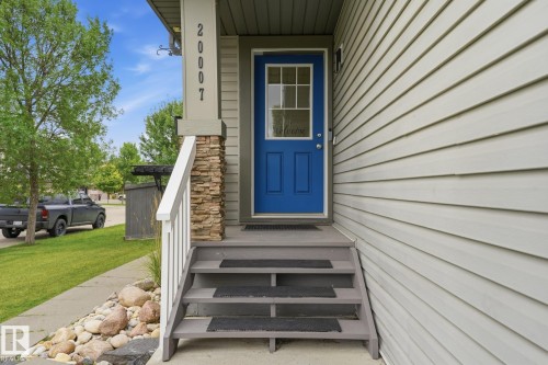 Entry featuring a vibrant blue door with upper lites, flanked by siding and a stone-accented column - 20007 131 Avenue Nw, Edmonton, AB 