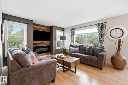 Wood-finish flooring throughout, multiple windows with blinds, feature wall with integrated television and fireplace, and a large picture window - 20007 131 Avenue Nw, Edmonton, AB 