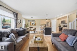 Open-concept living space featuring wood-finish flooring, a kitchen island with pendant lighting, stainless steel appliances, and light wood cabinetry - 