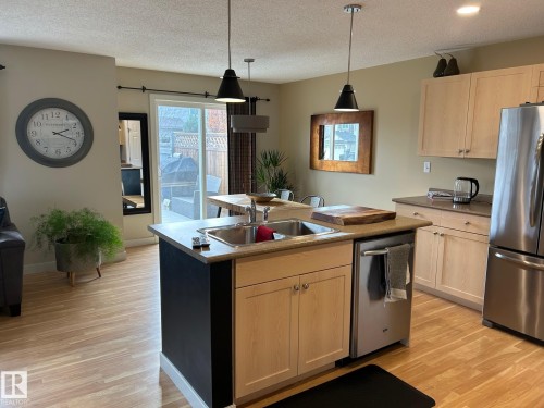 Kitchen featuring wood-finish flooring, light wood cabinetry, stainless steel appliances, and a kitchen island with a built-in sink - 20007 131 Avenue Nw, Edmonton, AB 
