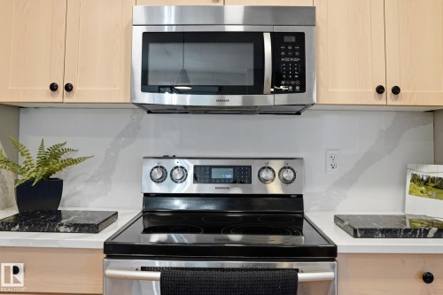 Stainless steel microwave, electric range with a smooth cooktop, light-toned cabinetry with black hardware, and a white countertop with a veined backsplash - 20007 131 Avenue Nw, Edmonton, AB 