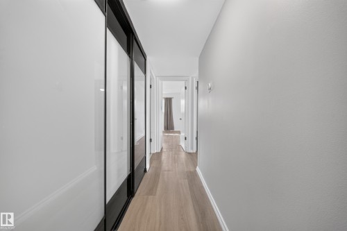 Hallway featuring wood-finish flooring, light gray walls, and sliding closet doors with black frames - 155 Marlborough Place Nw, Edmonton, AB 