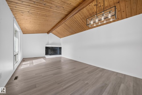 Vaulted wood-paneled ceiling with exposed beam, modern linear chandelier, corner fireplace with hearth, large window, and wood-finish flooring - 155 Marlborough Place Nw, Edmonton, AB 