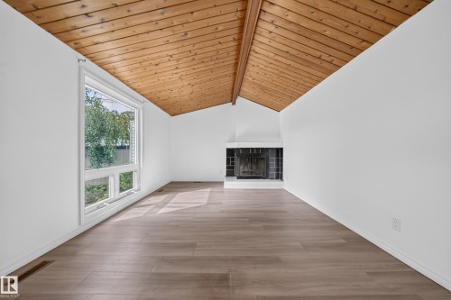 Vaulted wood-paneled ceiling, expansive window, light wood-finish flooring, white walls, and a fireplace with a white surround - 155 Marlborough Place Nw, Edmonton, AB 