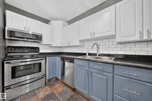 Kitchen featuring two-tone cabinetry, stainless steel appliances, black countertops, a subway tile backsplash, and stone tile flooring - 155 Marlborough Place Nw, Edmonton, AB 