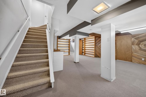 Carpeted staircase with white railings, recessed lighting, built-in shelving, wood-paneled accent wall, and neutral carpeting - 155 Marlborough Place Nw, Edmonton, AB 