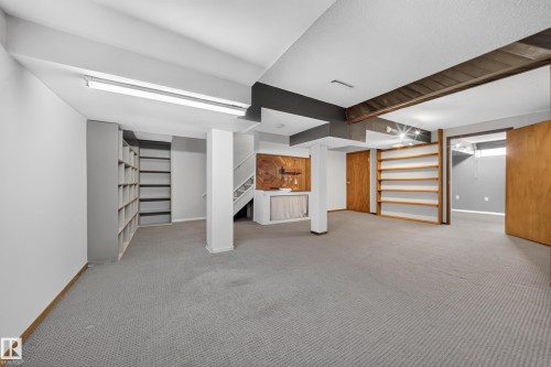Spacious room with gray carpeting, extensive built-in shelving, wood-paneled accents, and exposed ceiling beams - 155 Marlborough Place Nw, Edmonton, AB 