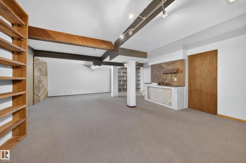 Open-concept room featuring wood-finish ceiling beams, track lighting, built-in shelving, a built-in bar with a wood-paneled backsplash, and carpet flooring - 155 Marlborough Place Nw, Edmonton, AB 
