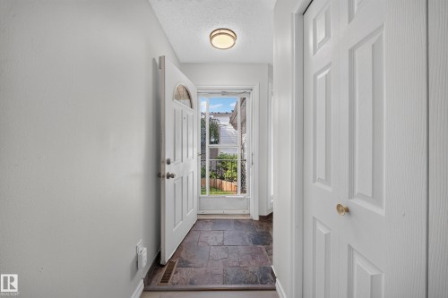 Foyer featuring slate tile flooring, a white paneled entry door with an arched glass insert, and a flush mount ceiling light - 155 Marlborough Place Nw, Edmonton, AB 