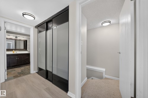 Wood-finish flooring, sliding frosted glass closet doors, bathroom with dark wood vanity, stone tile flooring in bathroom, and recessed ceiling lighting - 155 Marlborough Place Nw, Edmonton, AB 