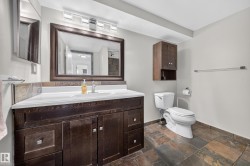 Dark wood-finish vanity with integrated sink, stone tile flooring, framed mirror, and wall-mounted cabinetry - 