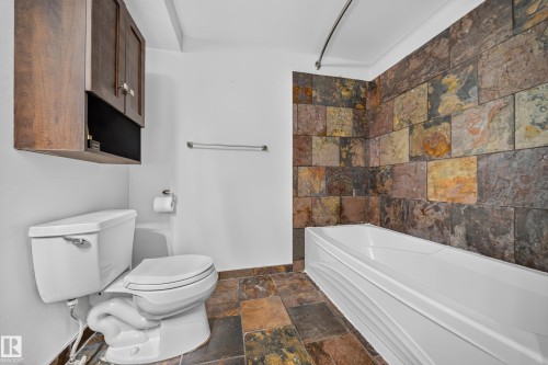 Bathroom featuring a built-in tub, extensive tile surround, wood-finish cabinetry, and a matching tile floor - 155 Marlborough Place Nw, Edmonton, AB 
