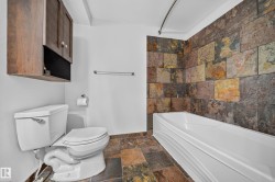 Bathroom featuring a built-in tub, extensive tile surround, wood-finish cabinetry, and a matching tile floor - 