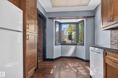 Wood-finish flooring with a bay window, wood cabinetry with decorative brass hardware, and a stone tile backsplash - 13351 109A Avenue Nw, Edmonton, AB 