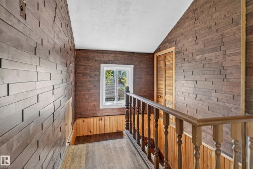 Bright upper-level hallway featuring exposed brick walls, wood-finish flooring, wooden railings with turned balusters, and a window with natural light - 13351 109A Avenue Nw, Edmonton, AB 