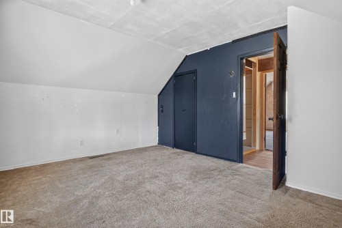 Carpeted room with sloped ceilings, a built-in closet with double doors, and a wood-finish interior door frame - 13351 109A Avenue Nw, Edmonton, AB 