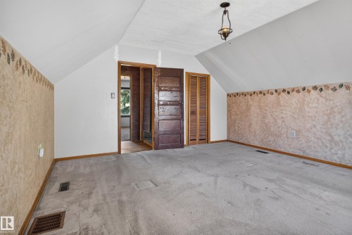 Sloped ceilings defining an expansive room with carpet flooring, a dark wood-finish door, and additional louvered closet doors - 13351 109A Avenue Nw, Edmonton, AB 